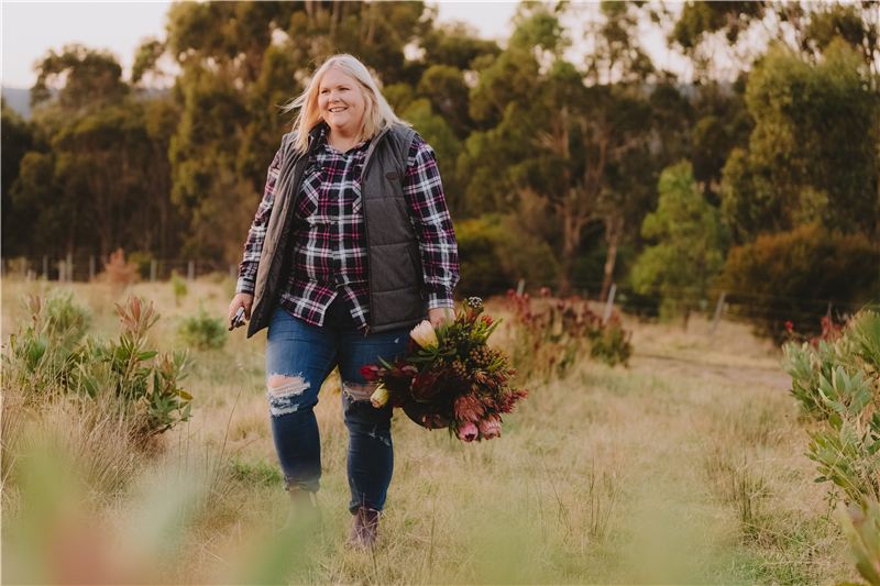 Nikki walking through the flower paddock carrying a bunch of natives