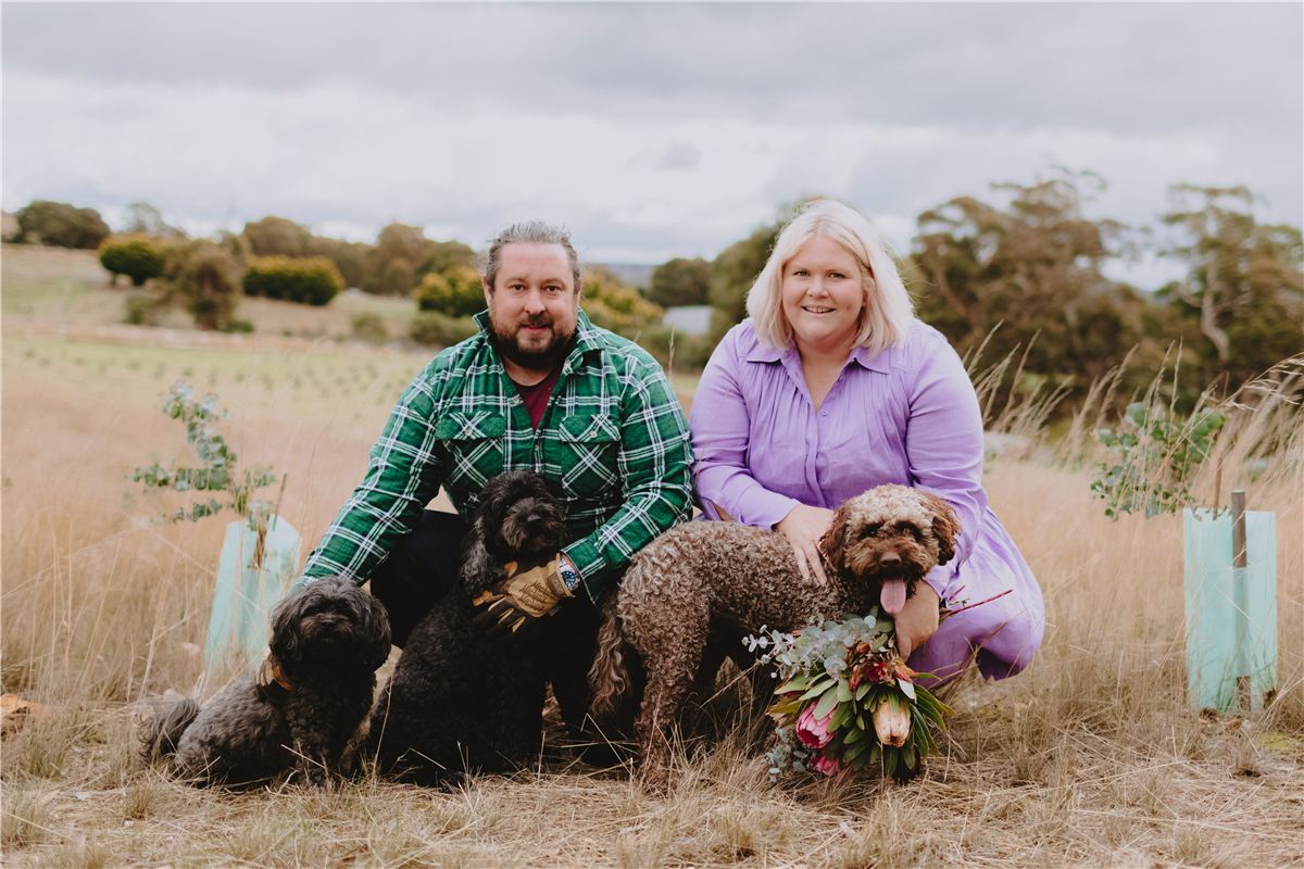 Sam and Nikki crouching in the paddock with their three dogs